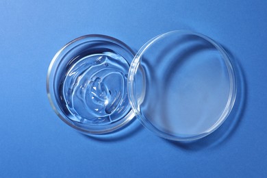 Photo of Petri dish with liquid and lid on blue background, flat lay