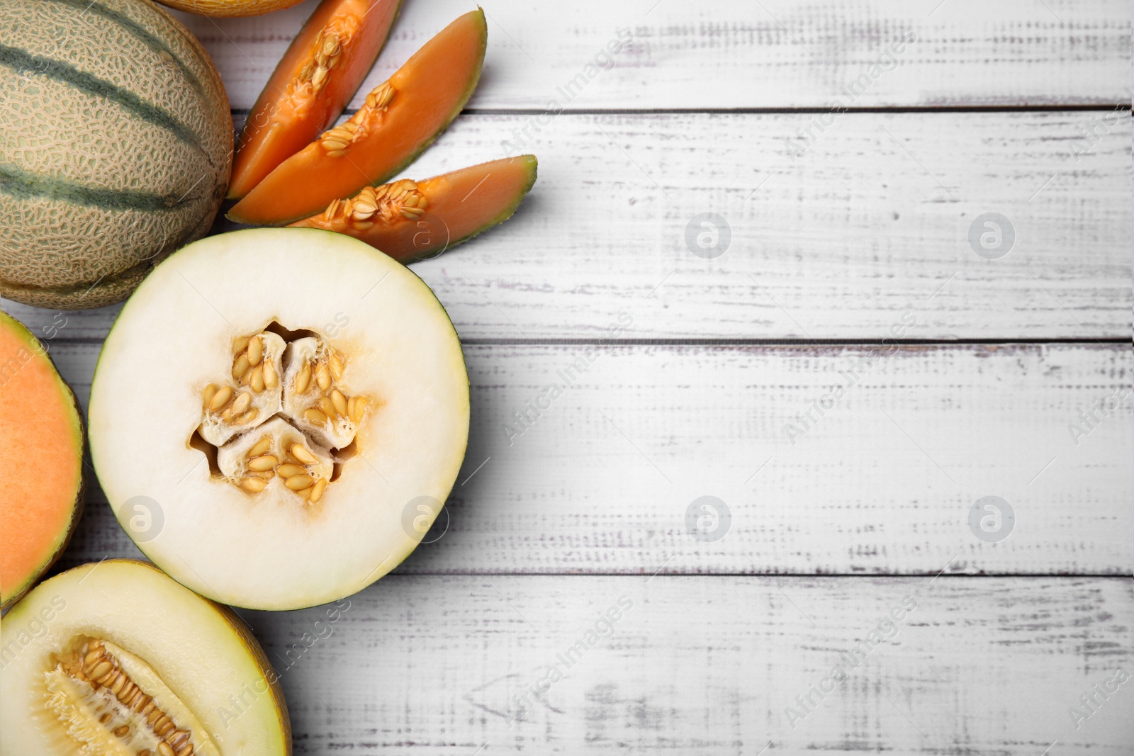 Photo of Tasty colorful ripe melons on white wooden table, flat lay. Space for text