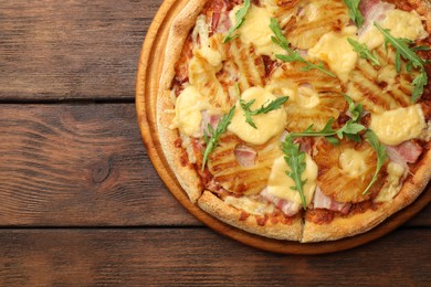 Photo of Delicious pineapple pizza with arugula on wooden table, top view. Space for text