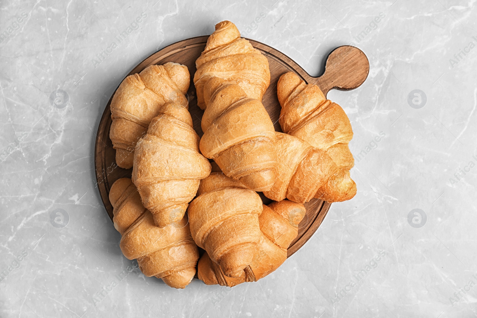 Photo of Wooden board with tasty croissants on light background, top view