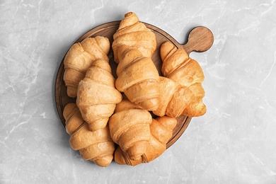 Wooden board with tasty croissants on light background, top view