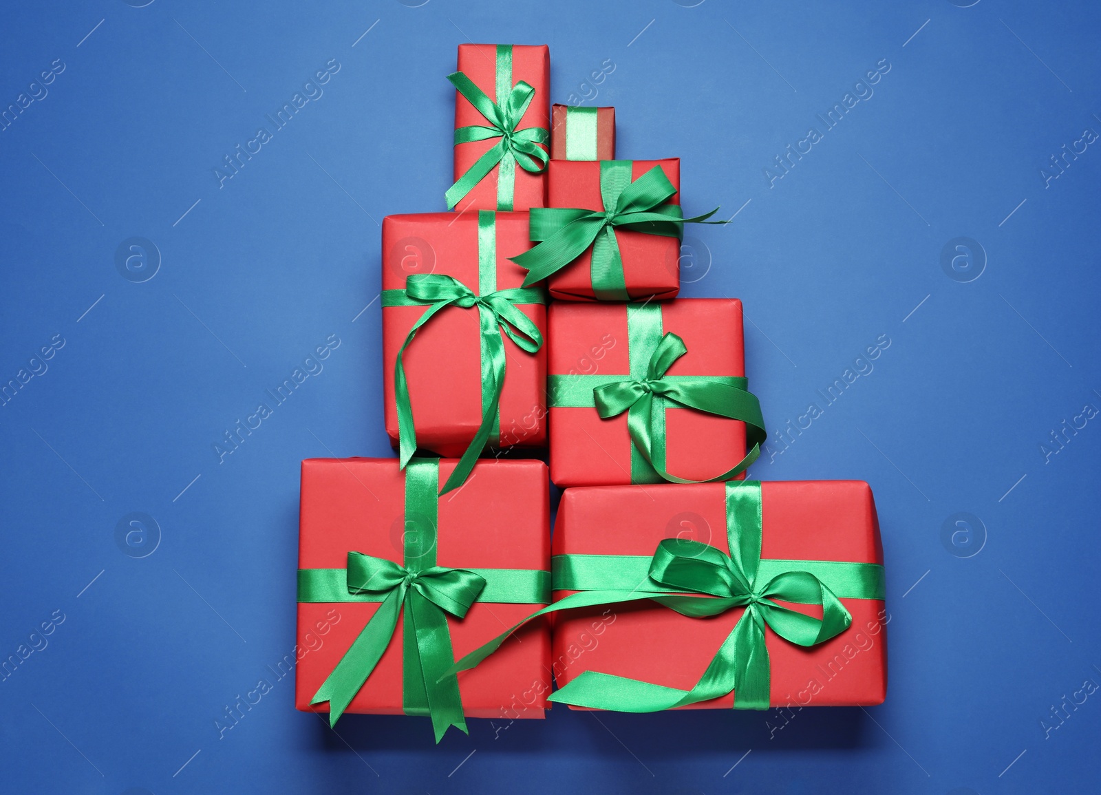 Photo of Christmas tree shape of gift boxes on blue background, flat lay