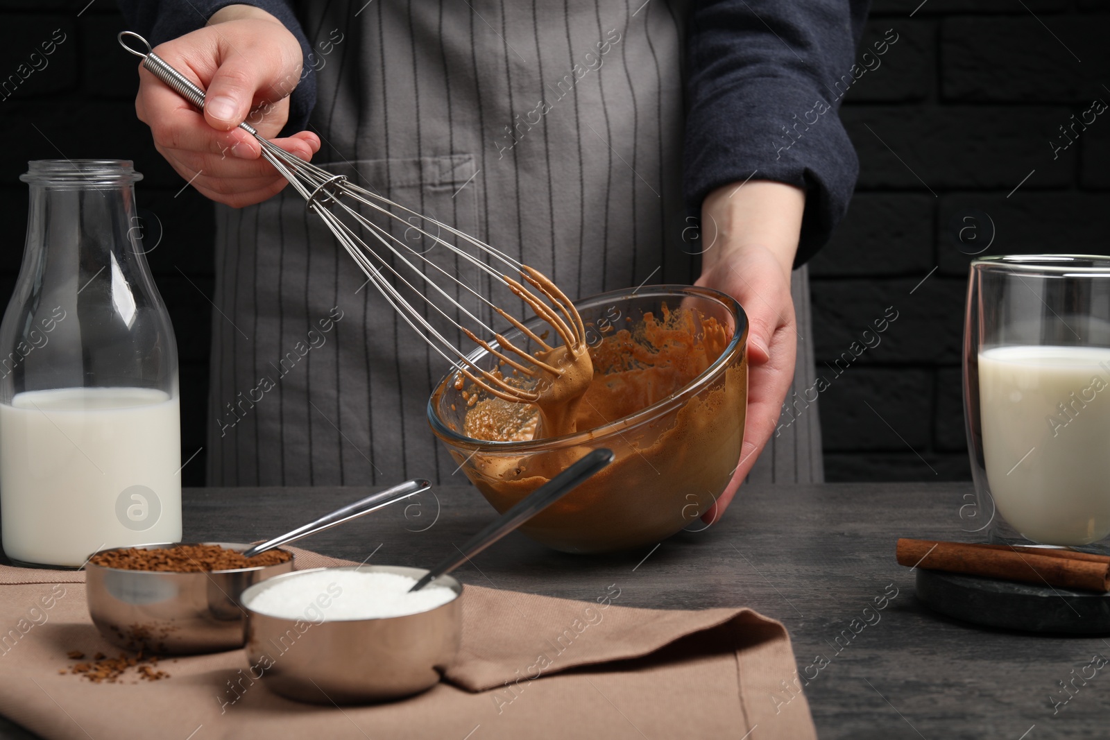 Photo of Woman whipping cream for dalgona coffee at grey table, closeup