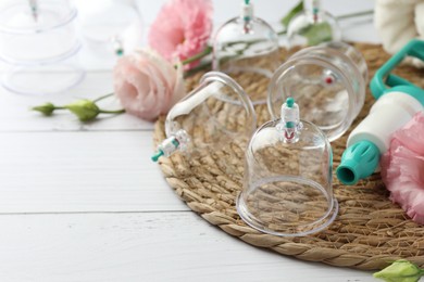Photo of Plastic cups, hand pump and flowers on white wooden table, space for text. Cupping therapy