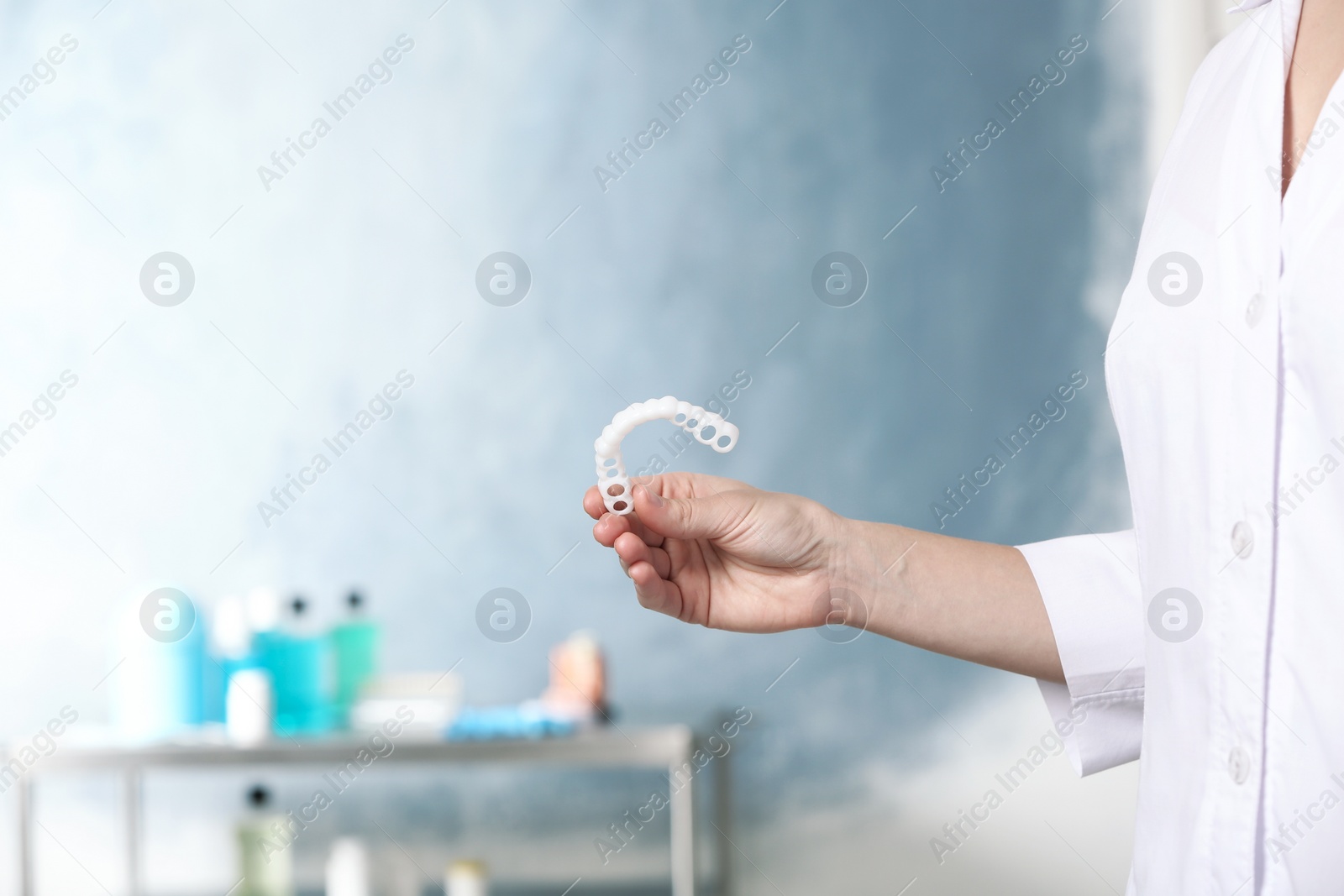 Photo of Dentist holding teeth cover on blurred background, closeup. Space for text