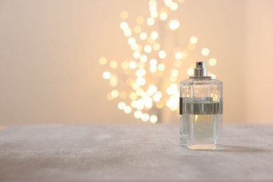 Photo of Bottle of perfume on table against beige background with blurred lights, space for text