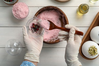 Photo of Woman in gloves making bath bomb at white wooden table, top view