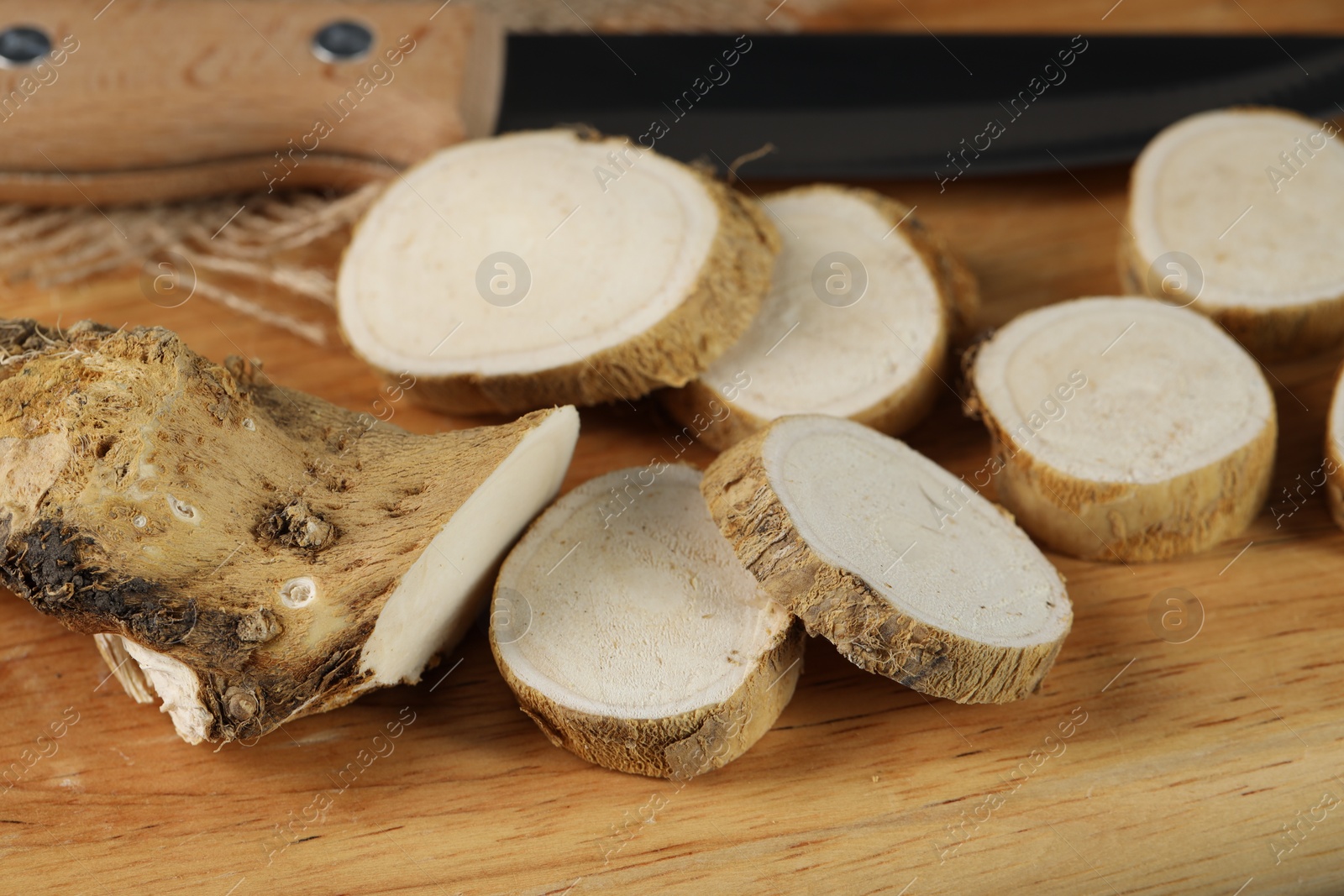 Photo of Cut horseradish root and knife on wooden board, closeup