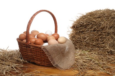 Photo of Wicker basket full of chicken eggs and dried straw on wooden table against white background