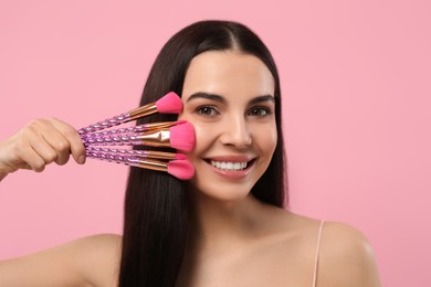 Photo of Happy woman with different makeup brushes on pink background