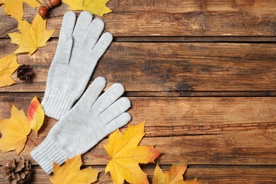 Stylish woolen gloves and dry leaves on wooden table, flat lay. Space for text