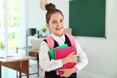 Girl wearing school uniform with backpack in classroom