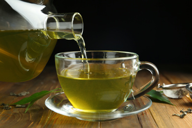 Pouring green tea into cup at wooden table