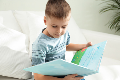 Photo of Little boy reading book on sofa indoors