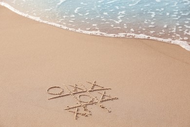 Tic tac toe game drawn on sand near sea, space for text