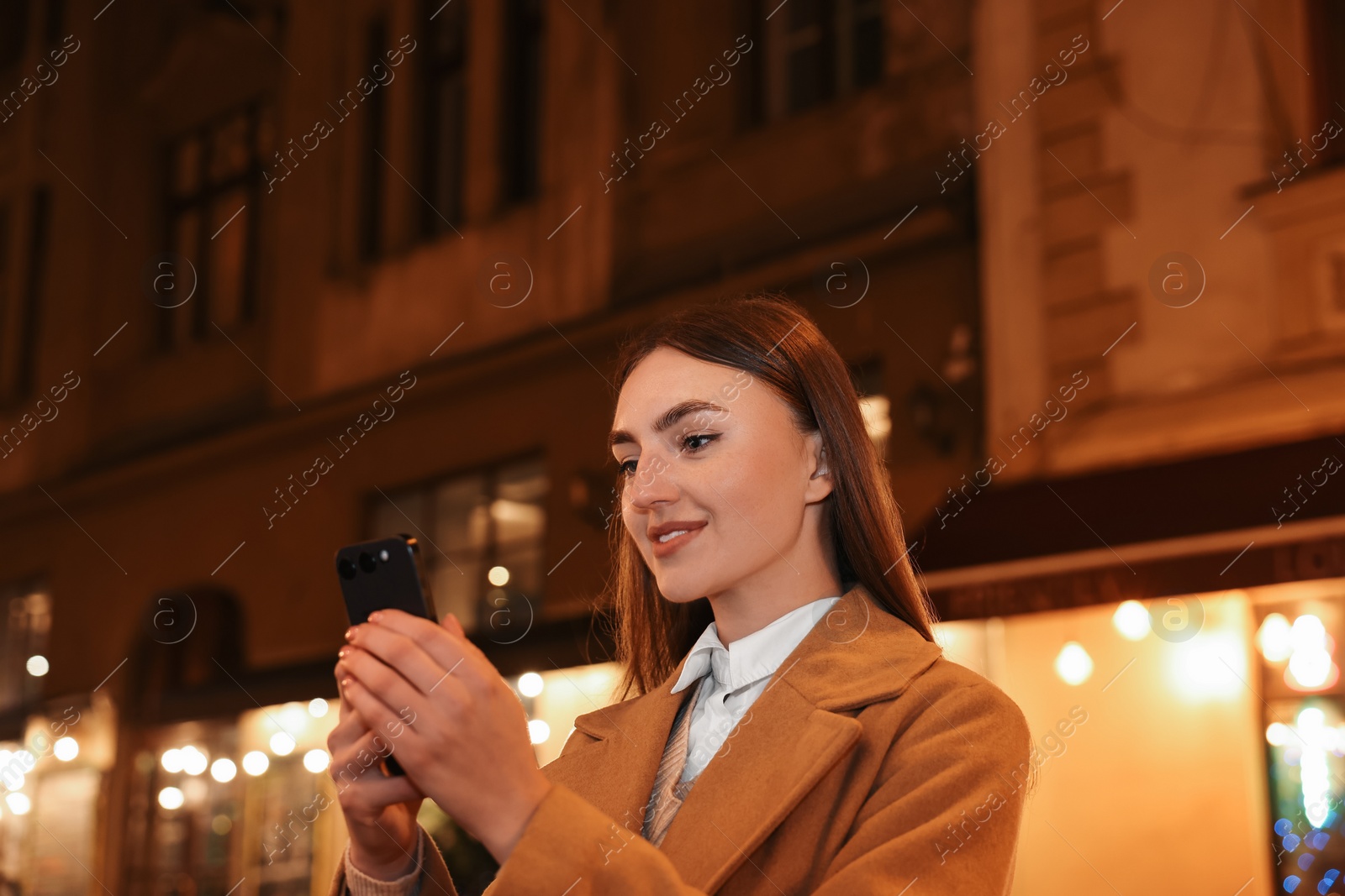 Photo of Smiling woman using smartphone on night city street