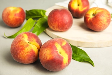 Photo of Tasty fresh peaches, leaves and stone board on grey table