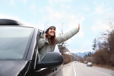 Happy woman leaning out of car window on road. Winter vacation