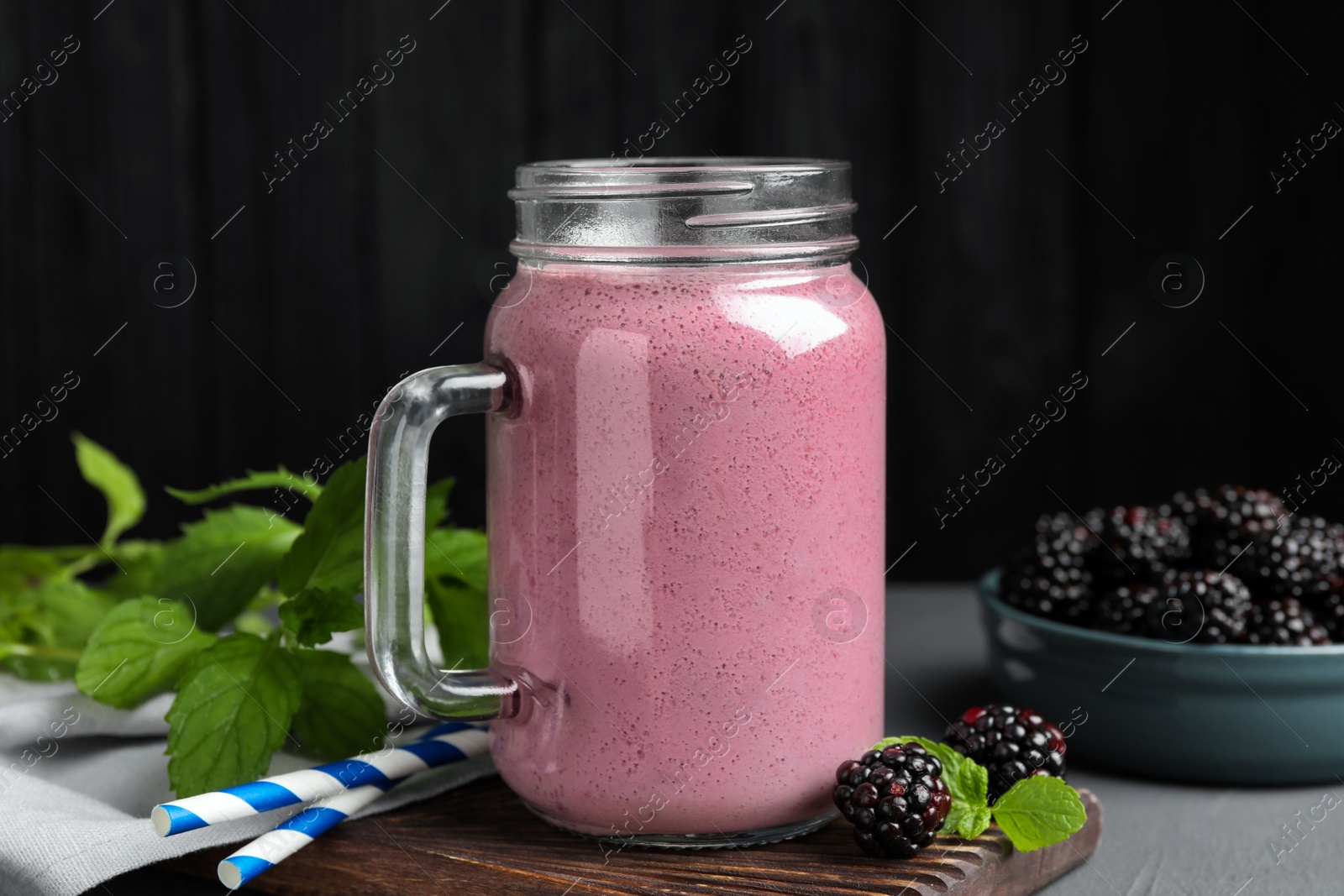 Photo of Mason jar of blackberry smoothie, mint and berries on grey table