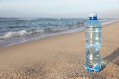 Plastic bottle of fresh water on wet sand near sea. Space for text