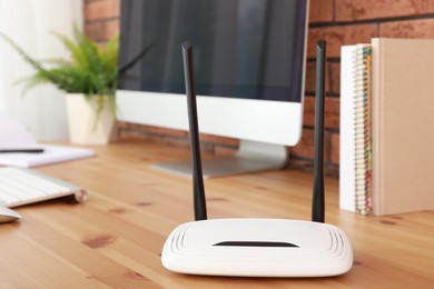 Photo of Modern wi-fi router near computer on wooden table