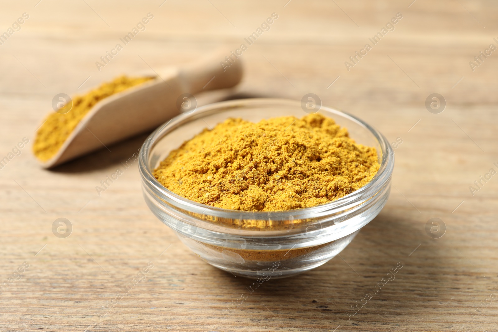 Photo of Curry powder in bowl and scoop on wooden table, closeup