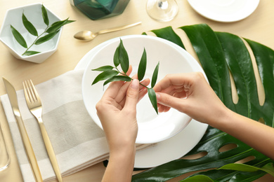 Photo of Woman setting table with green leaves for festive dinner, above view