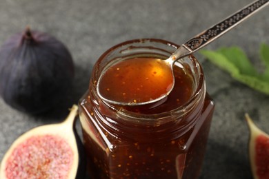Photo of Glass jar of tasty fig jam with spoon on grey table, closeup