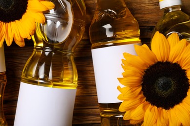 Bottles of sunflower cooking oil and beautiful flowers on wooden table, top view