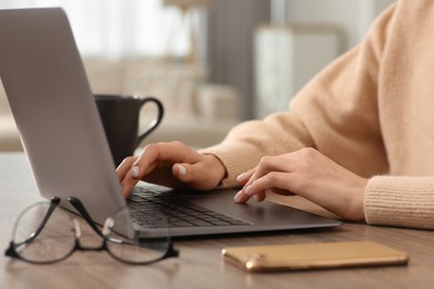 Woman working with laptop at wooden desk indoors, closeup