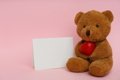 Photo of Cute teddy bear with red heart and blank card on pink background, space for text. Valentine's day celebration