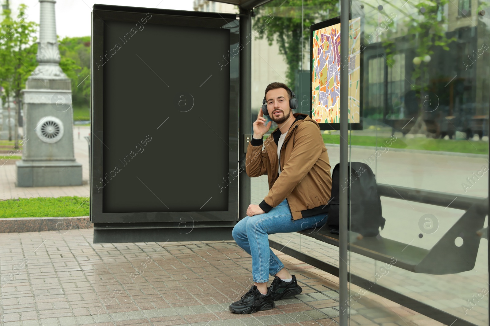 Image of Young man listening to music while waiting for public transport at bus stop