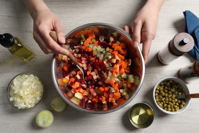 Photo of Woman preparing tasty vinaigrette salad at light wooden table, top view