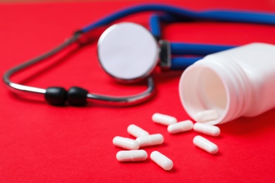 Photo of Scattered pills, container and stethoscope on color background. Heart disease concept