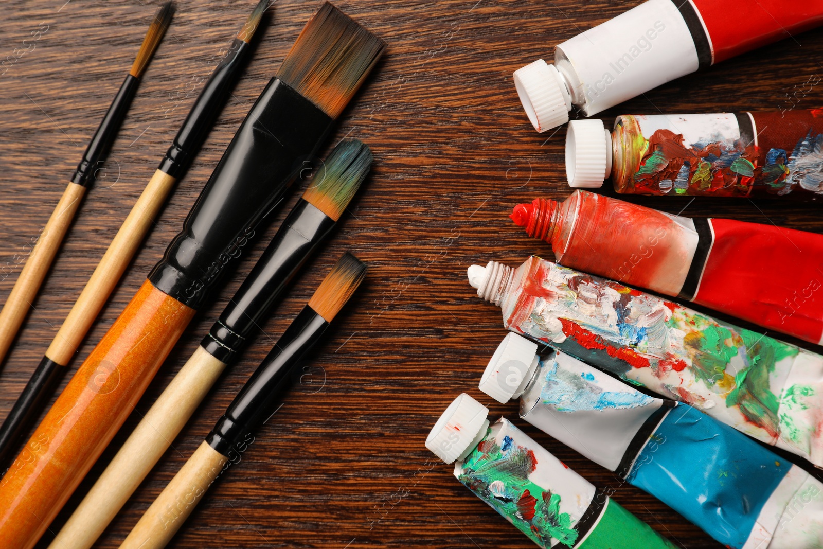 Photo of Tubes with oil paints and brushes on wooden table, flat lay