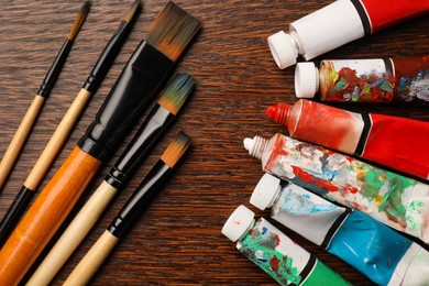 Tubes with oil paints and brushes on wooden table, flat lay