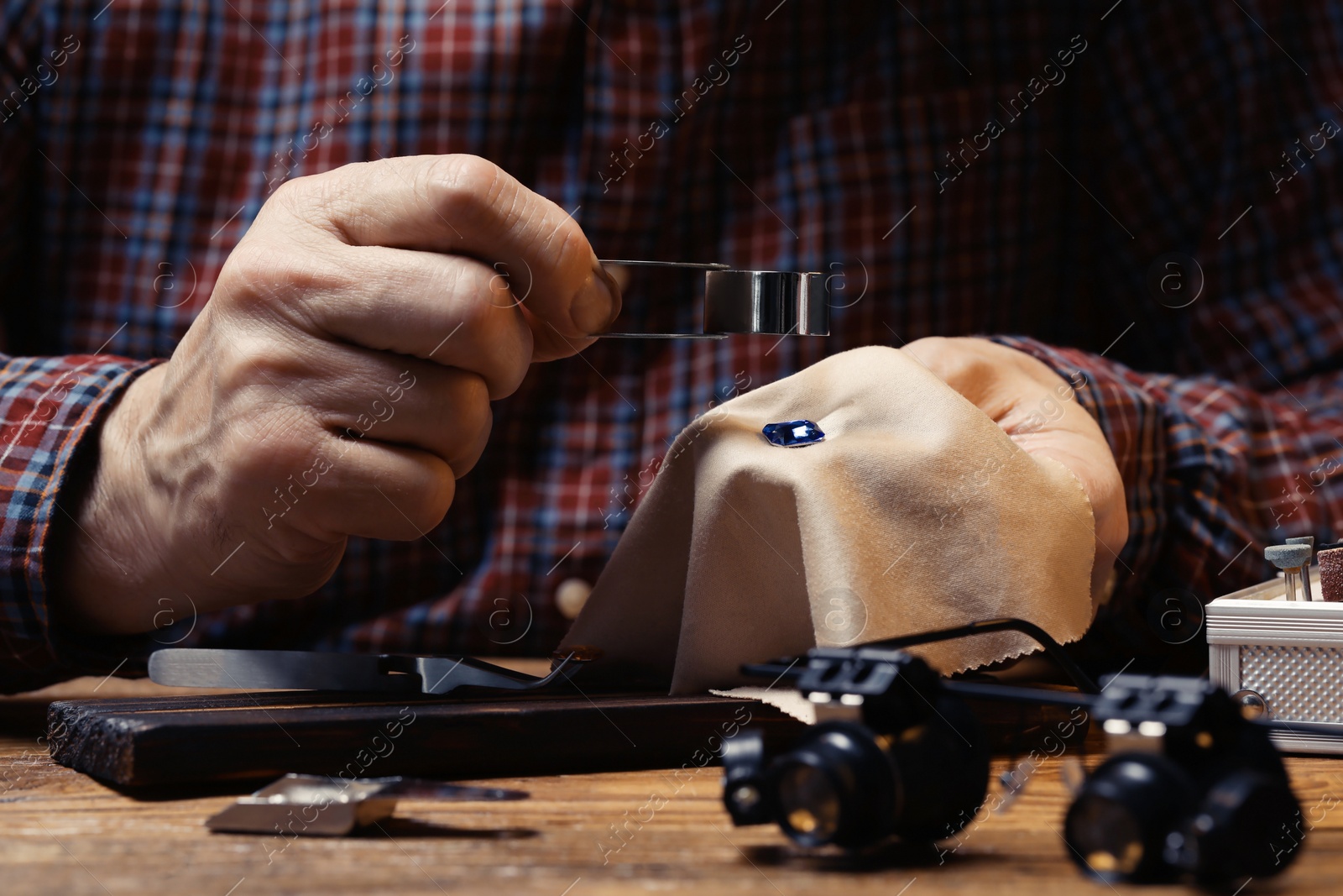 Photo of Professional jeweler working with gemstone at wooden table, closeup