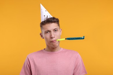 Young man in party hat with blower on orange background