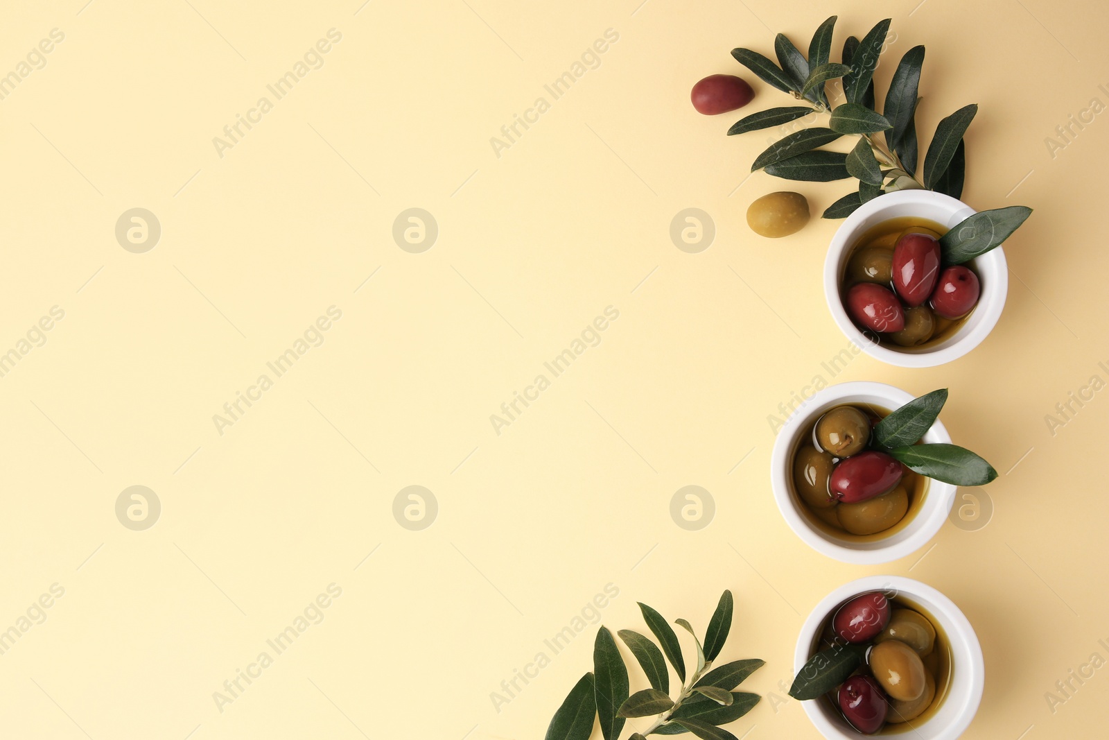 Photo of Bowls with different ripe olives and leaves on beige background, flat lay. Space for text