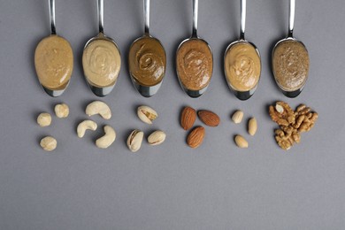 Photo of Tasty nut butters in spoons and raw nuts on gray table, flat lay. Space for text