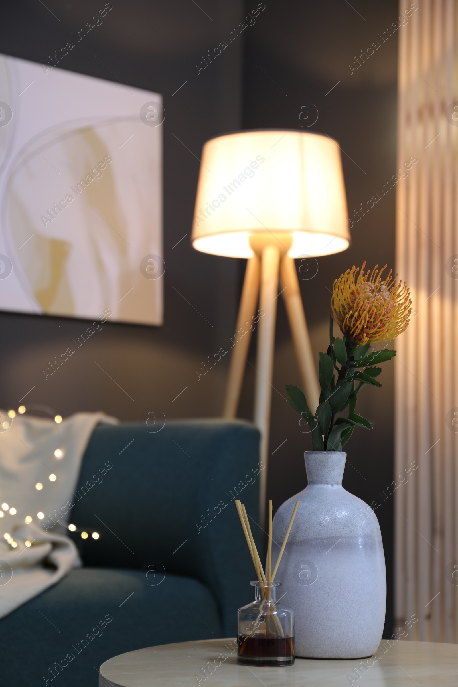 Photo of Vase with beautiful flower and air freshener on wooden coffee table near sofa in room