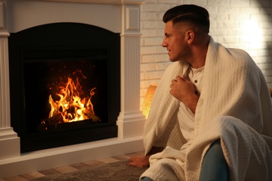Photo of Man covered with white plaid sitting at fireplace