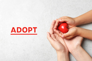 Woman and child holding heart on grey stone background, top view. Adoption concept