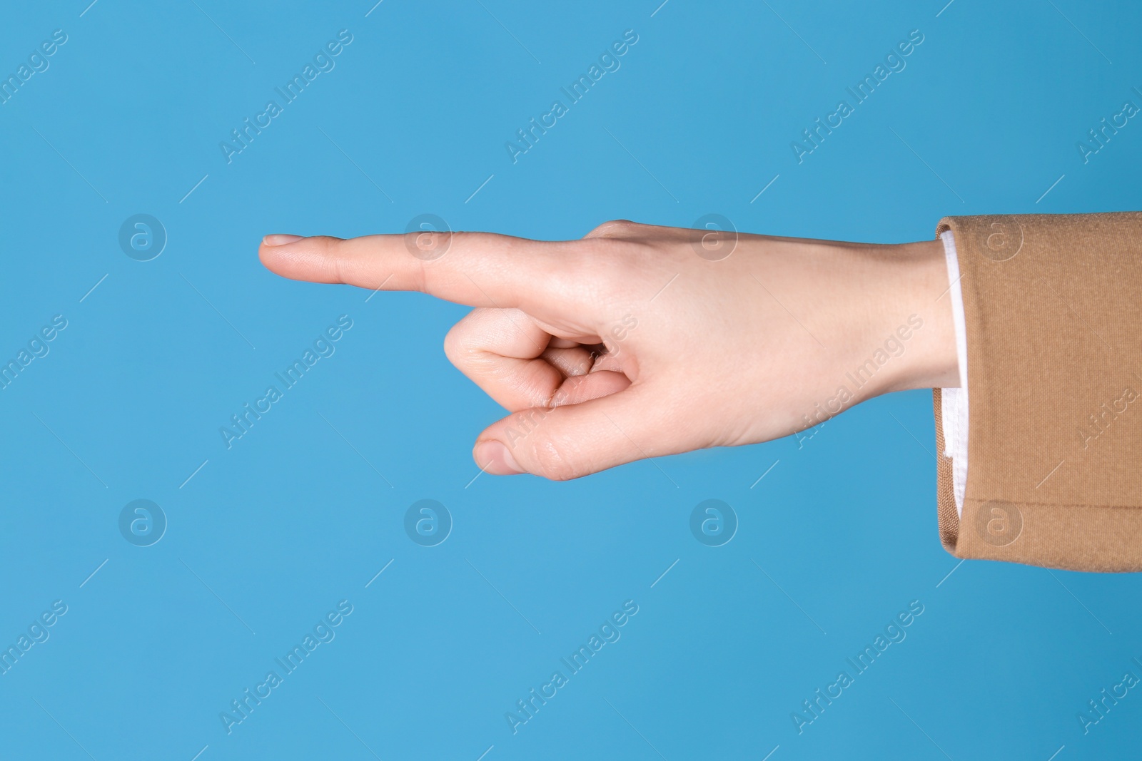 Photo of Businesswoman pointing at something on light blue background, closeup. Finger gesture