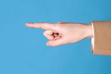 Photo of Businesswoman pointing at something on light blue background, closeup. Finger gesture