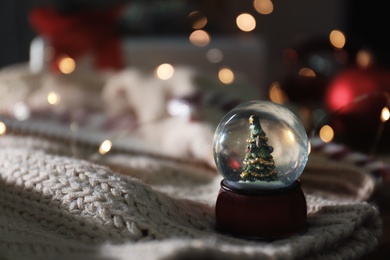 Photo of Christmas snow globe with knitting clothes on blurred background. Space for text