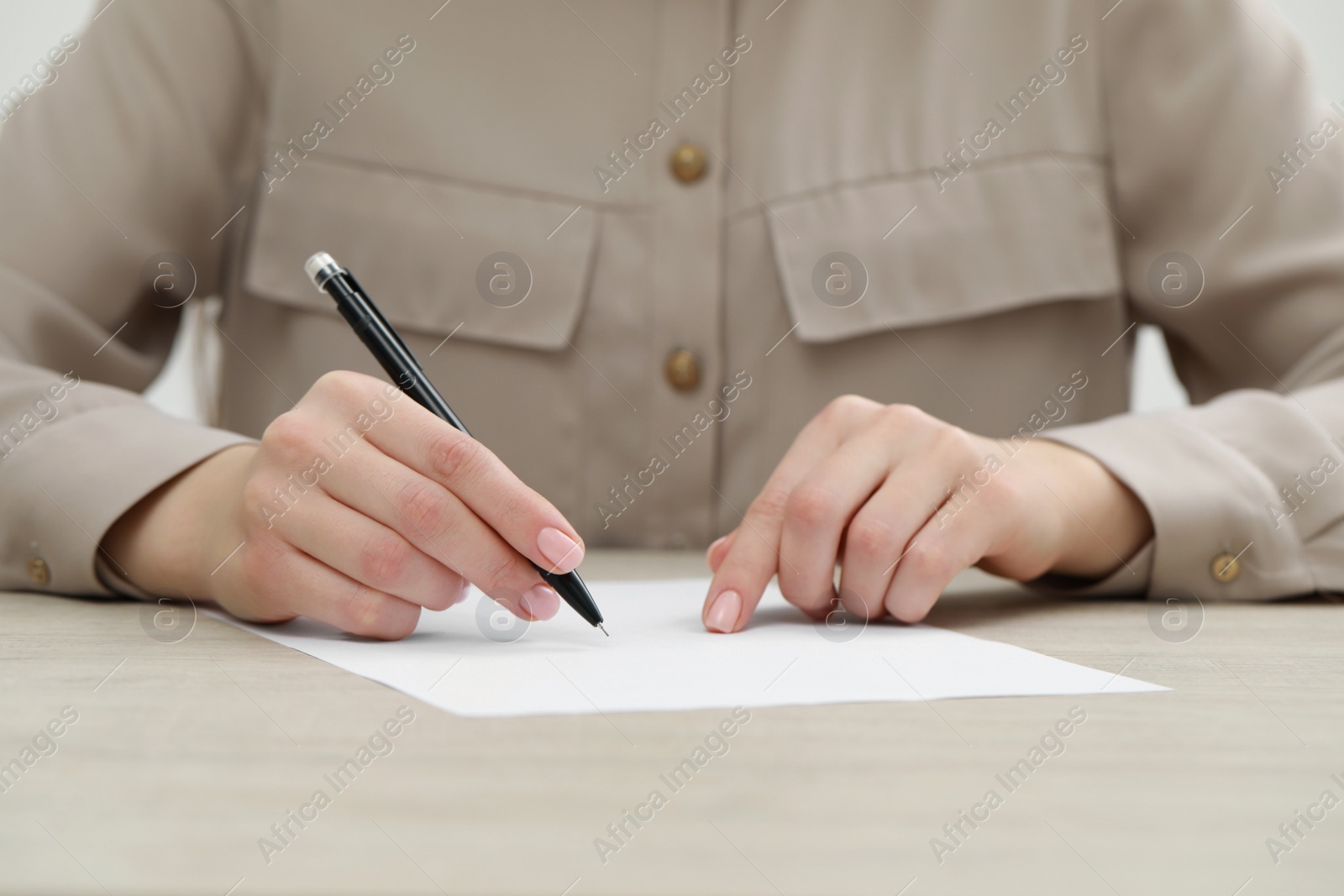 Photo of Woman writing on sheet of paper at light wooden table, closeup