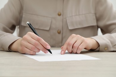 Photo of Woman writing on sheet of paper at light wooden table, closeup