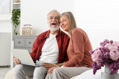 Photo of Senior couple using laptop on sofa at home