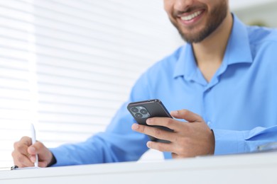 Photo of Man using smartphone while working at white table in office, closeup